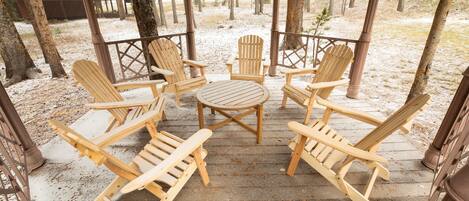 A wooden deck with Adirondack chairs and a table, surrounded by trees.