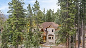 A house surrounded by tall pine trees, with a stone pathway leading to the entrance. - Sleeps 20 | Hot Tub + Game Room & Theater | Steps to Ski Shuttle | River Rock (Breckenridge)