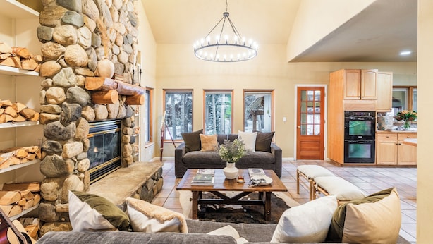 A spacious living room with a stone fireplace, a large chandelier, and a cozy seating area. - Sleeps 20 | Hot Tub + Game Room & Theater | Steps to Ski Shuttle | River Rock (Breckenridge)