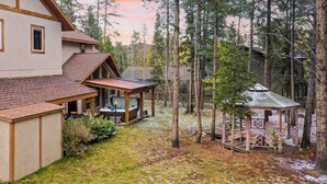 A two-story house with a covered patio and a gazebo in a forested area. - Sleeps 20 | Hot Tub + Game Room & Theater | Steps to Ski Shuttle | River Rock (Breckenridge)