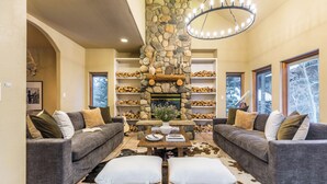 A cozy living room with two grey sofas, a stone fireplace, and a chandelier. - Sleeps 20 | Hot Tub + Game Room & Theater | Steps to Ski Shuttle | River Rock (Breckenridge)