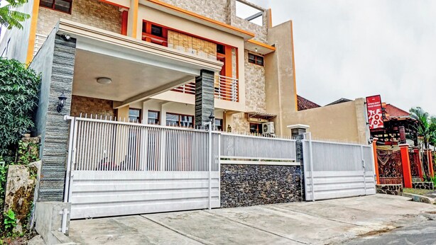 A modern two-story house with a stone facade, a balcony, and a gated entrance. - OYO 90383 Avisha Guest House Syariah (Malang)