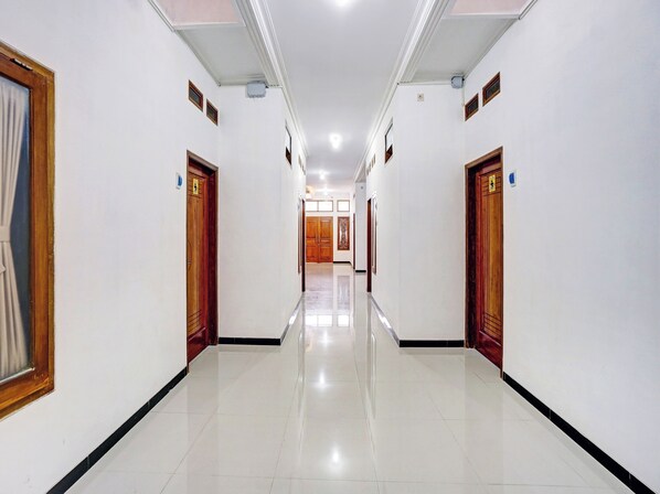 A hotel corridor with doors on both sides, a tiled floor, and a ceiling with recessed lighting.