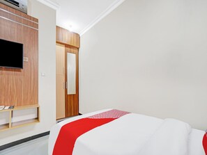 A hotel room with a bed, a TV mounted on the wall, and a wardrobe.