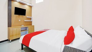 A hotel room with a bed, a TV mounted on a wooden panel, a small desk, and an air conditioning unit. - OYO 90383 Avisha Guest House Syariah (Malang)