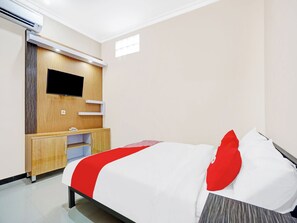 Hotellihuone, jossa on sänky, puupaneeliin asennettu televisio, pieni työpöytä ja ilmastointilaite.