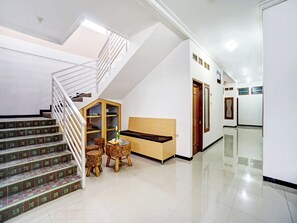 A clean, modern interior with a staircase, a wooden cabinet, a round table with chairs, and a sofa. - OYO 90383 Avisha Guest House Syariah (Malang)