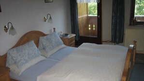 Un dormitorio con una cama de madera, dos almohadas, una mesita de noche, una lámpara y una ventana con cortinas.