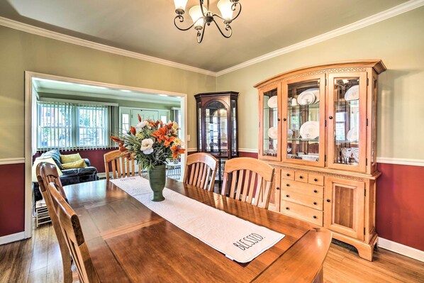 A dining room with a wooden table, chairs, a vase with flowers, and a china cabinet.