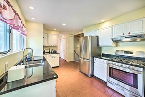 A kitchen with white cabinets, stainless steel appliances, a black countertop, and a tiled floor.