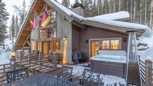 A log cabin with a hot tub, deck chairs, and flags. - Private Ski in/out Lodge! Hot Tub, 2 King En Suites, Stunning Views (Mountain Village)