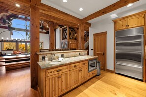 Une cuisine avec des meubles en bois, un réfrigérateur en acier inoxydable et une grande fenêtre donnant sur la forêt.