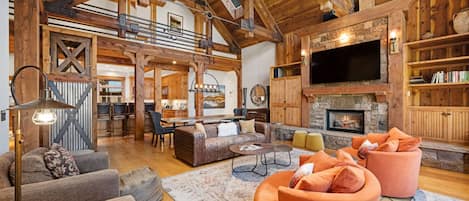 A spacious living area with a fireplace, wooden beams, and a television mounted above it.
