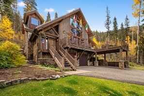 A large wooden cabin with multiple levels, a stone foundation, and a covered porch.