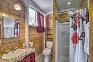 Ein Badezimmer mit Holzwänden, einem weißen Waschbecken, einer Toilette und einer Duschvorhang mit Blumenmuster.