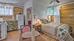 A cozy room with a bed, a nightstand, a lamp, a chair, a small table, and a ceiling fan. - Cozy Pahoa Hideaway Near Black-Sand Beaches! (Pahoa)