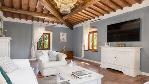 Amplia sala de estar con un sofá blanco, una mesa de centro blanca y un mueble blanco. Hay un televisor de pantalla plana grande montado en la pared.