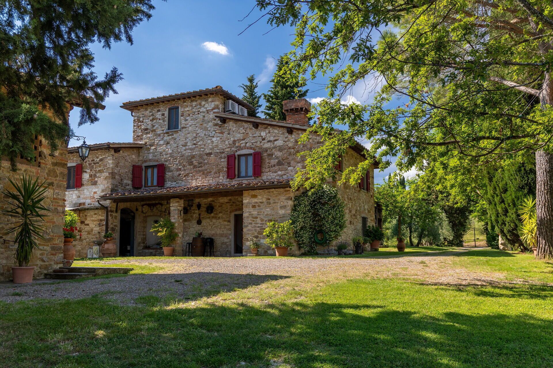 Una casa in pietra con tetto in tegole, persiane rosse e vialetto sterrato.