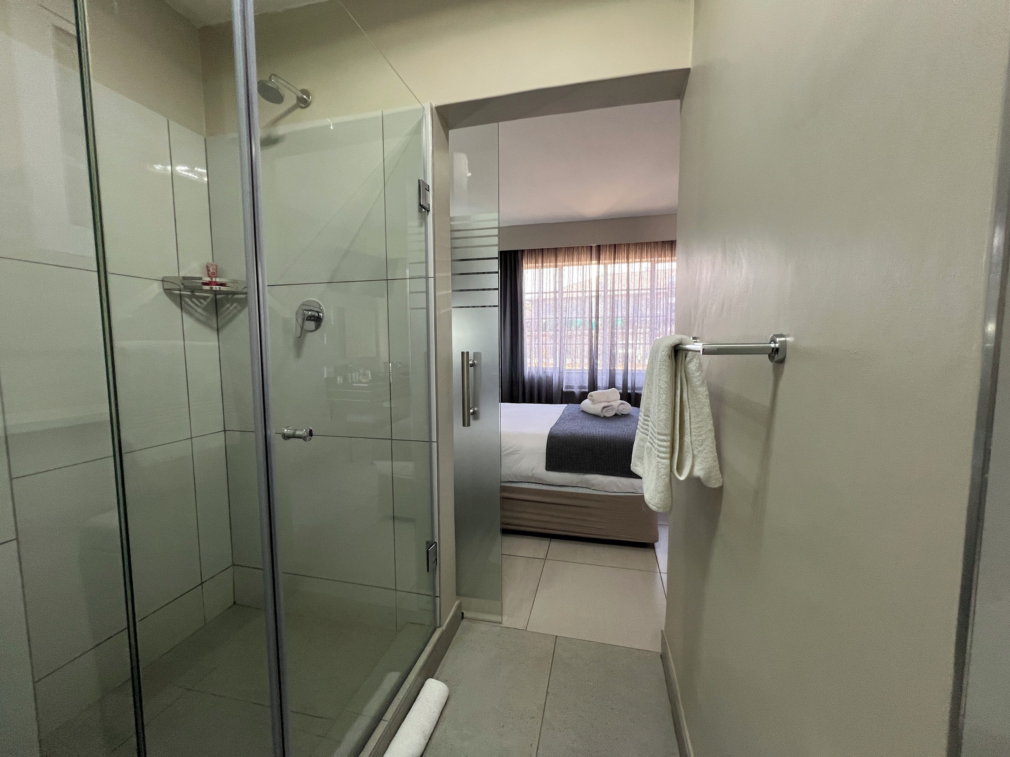 A modern bathroom with a glass shower enclosure, a visible towel rack, and a bed with a neatly folded towel.