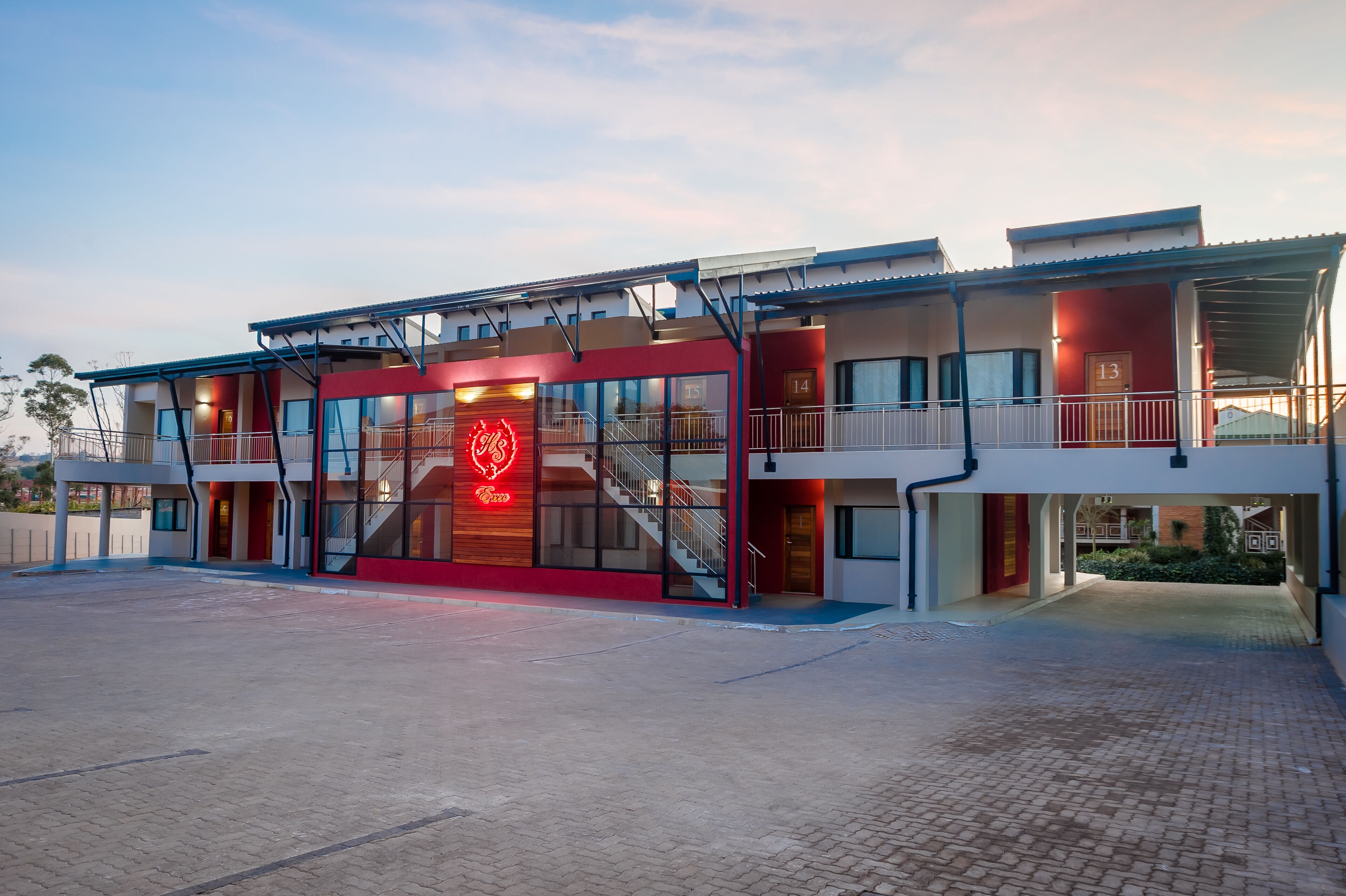 Un hôtel moderne à la façade rouge et blanche, doté de nombreux balcons et d’une enseigne lumineuse bien visible.