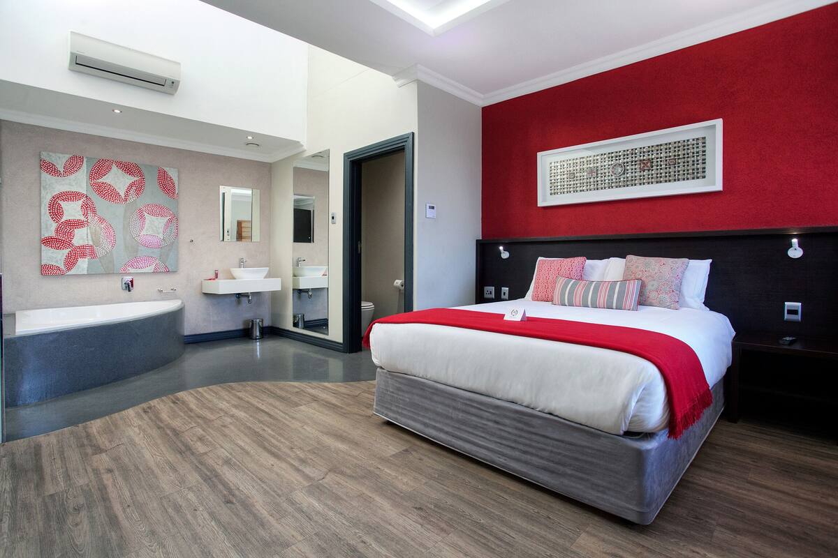 Een moderne hotelkamer met een groot bed, een badkamer met bad en een rode accentmuur.