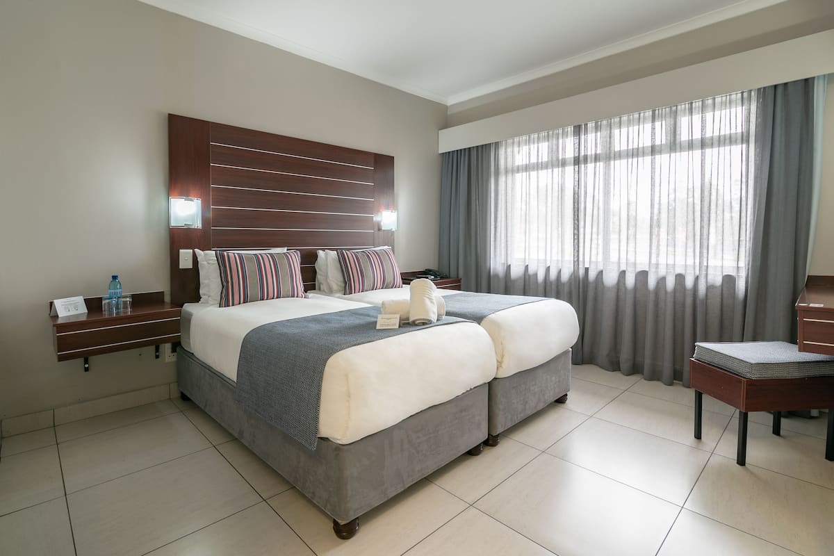 Hotelkamer met een groot bed, een houten hoofdeinde, een nachtkastje, een stoel en een raam met gordijnen.