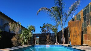 A swimming pool with a stone border, surrounded by palm trees and a wooden fence.