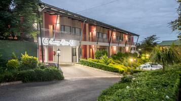 A multi-story hotel with a balcony on the second floor, a well-maintained garden, and a clear driveway.
