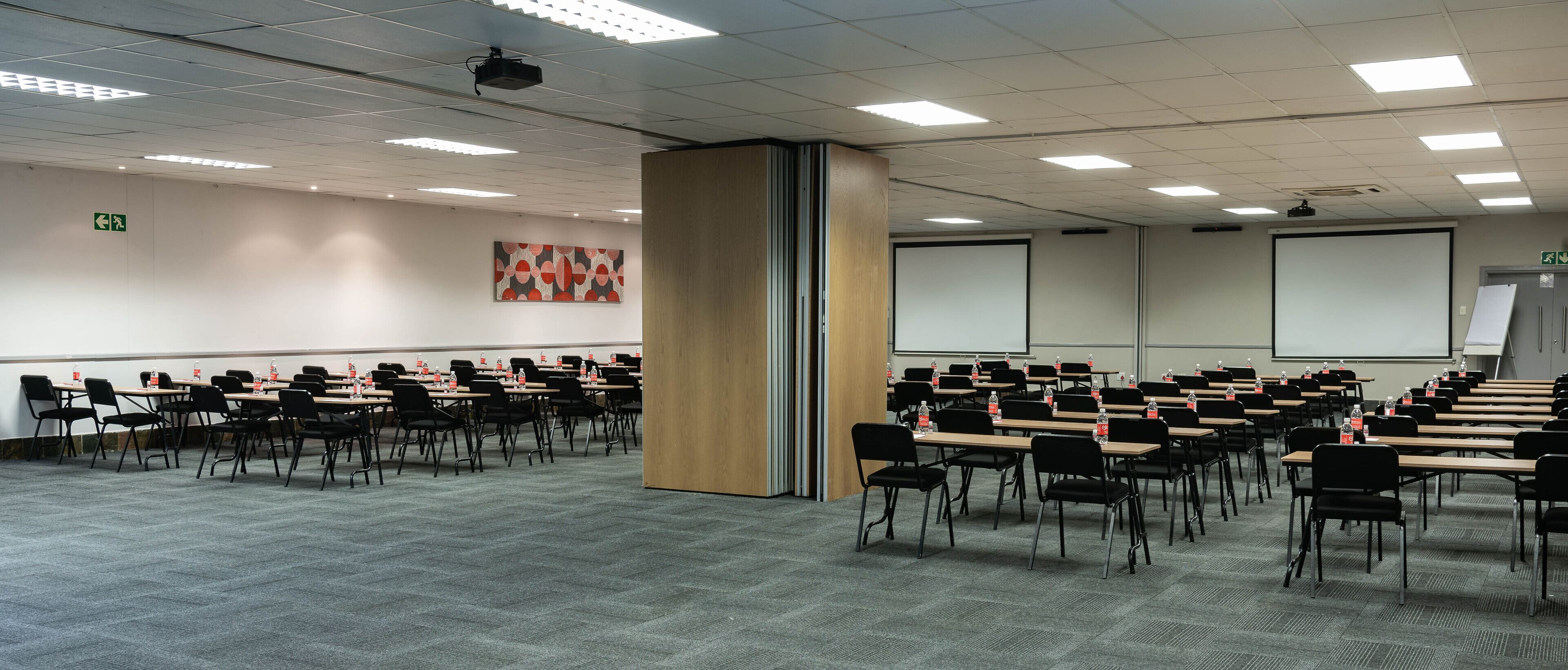 Une salle de conférence avec des rangées de tables et de chaises, un projecteur et un écran.
