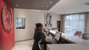 A reception desk with a receptionist, a large window, and a red wall with a decorative emblem.