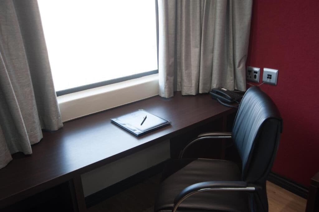 Un escritorio con una laptop, una silla y una ventana con cortinas.