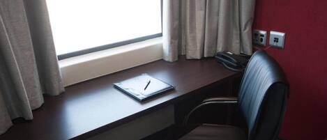 Un escritorio con una laptop, una silla y una ventana con cortinas.
