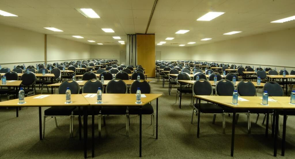 A conference room with rows of tables and chairs, equipped with water bottles.