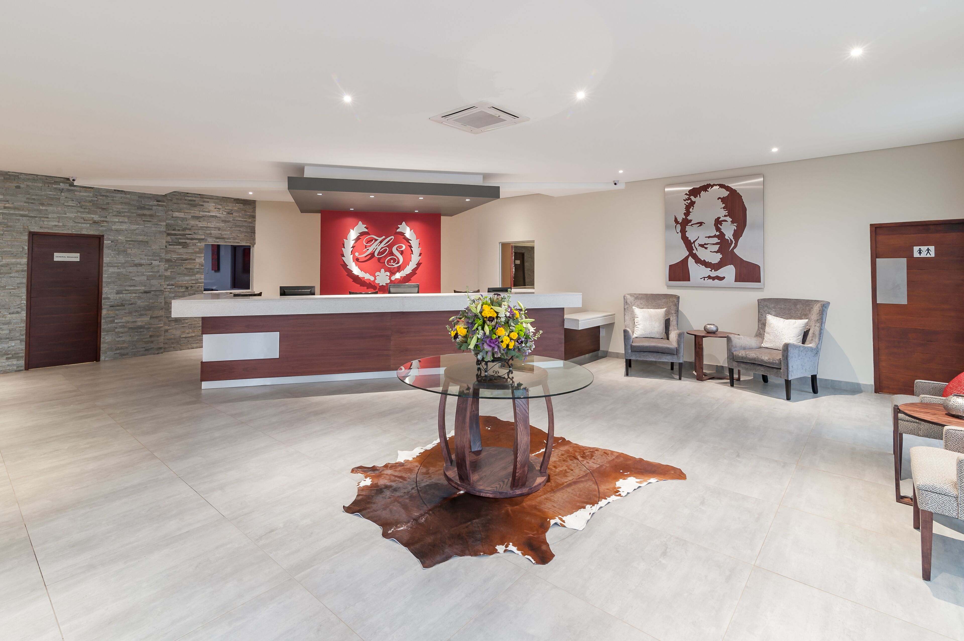 A modern reception area with a glass-top desk, a red logo, and a large portrait on the wall.