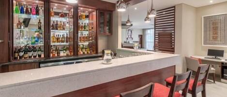 A bar area with a long counter, multiple shelves of bottles, and hanging pendant lights.