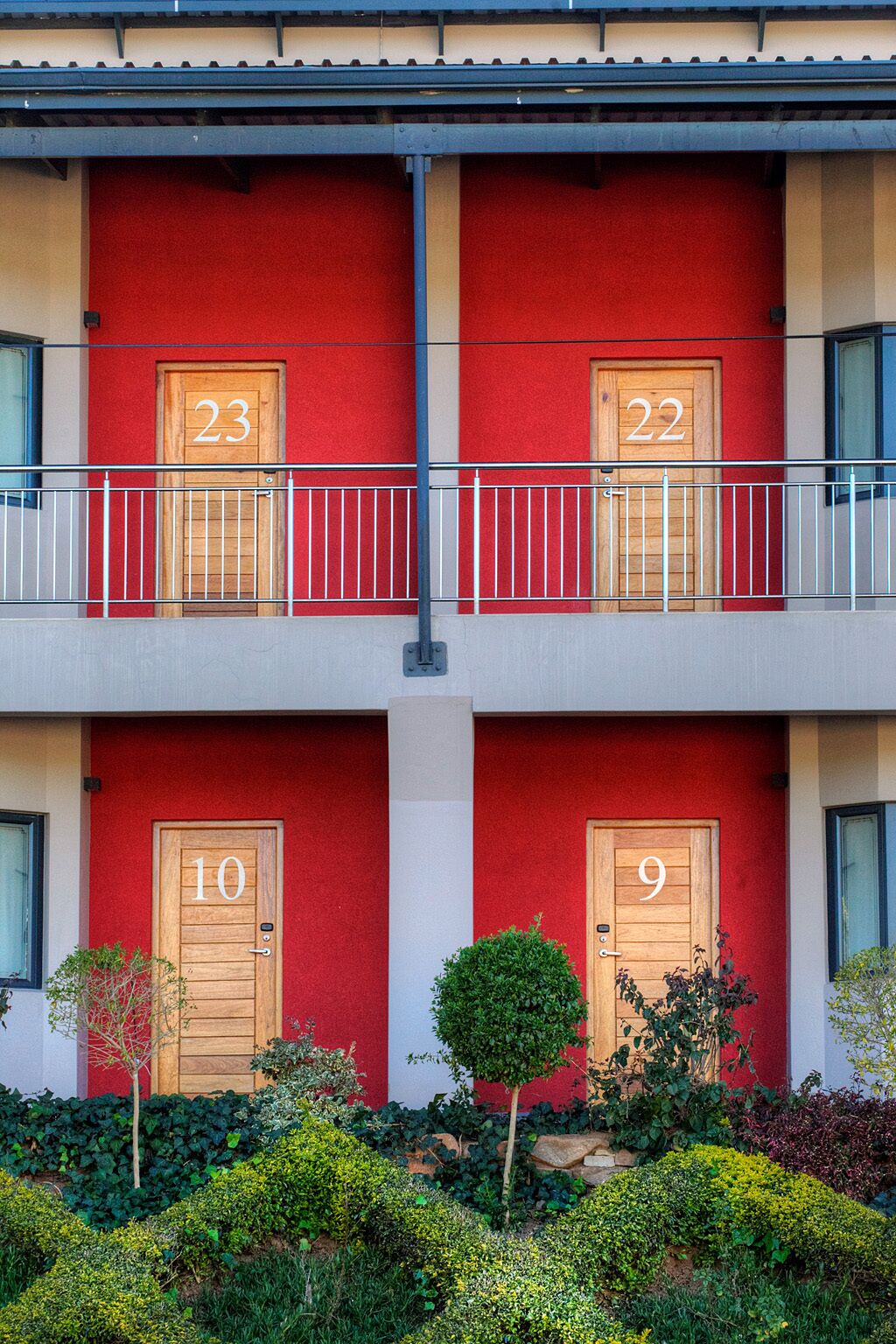 Un immeuble à la façade rouge, avec des portes numérotées et un balcon doté d’une rambarde en métal.