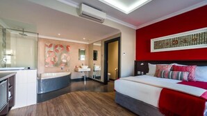 A modern hotel room with a large bed, a bathroom with a bathtub, and a red accent wall.