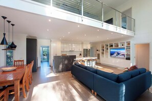 A modern open-plan living space with a dining area, kitchen, and a large TV mounted on the wall. - The Gums - Echuca Holiday Homes (Echuca)
