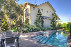 A two-story house with a swimming pool, surrounded by trees and shrubs.