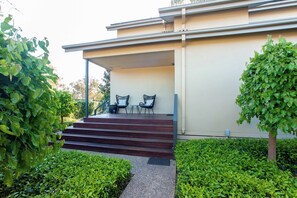 Um edifício moderno com área de estar coberta ao ar livre, degraus de acesso e vegetação bem cuidada.