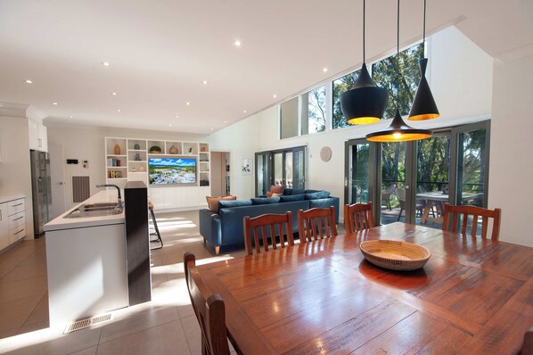 A modern kitchen with a central island, a dining area with a wooden table and chairs, and a living area with a blue sofa.