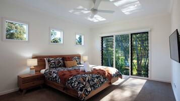 A bedroom with a large bed, two bedside tables, a ceiling fan, and a view of trees through the window.