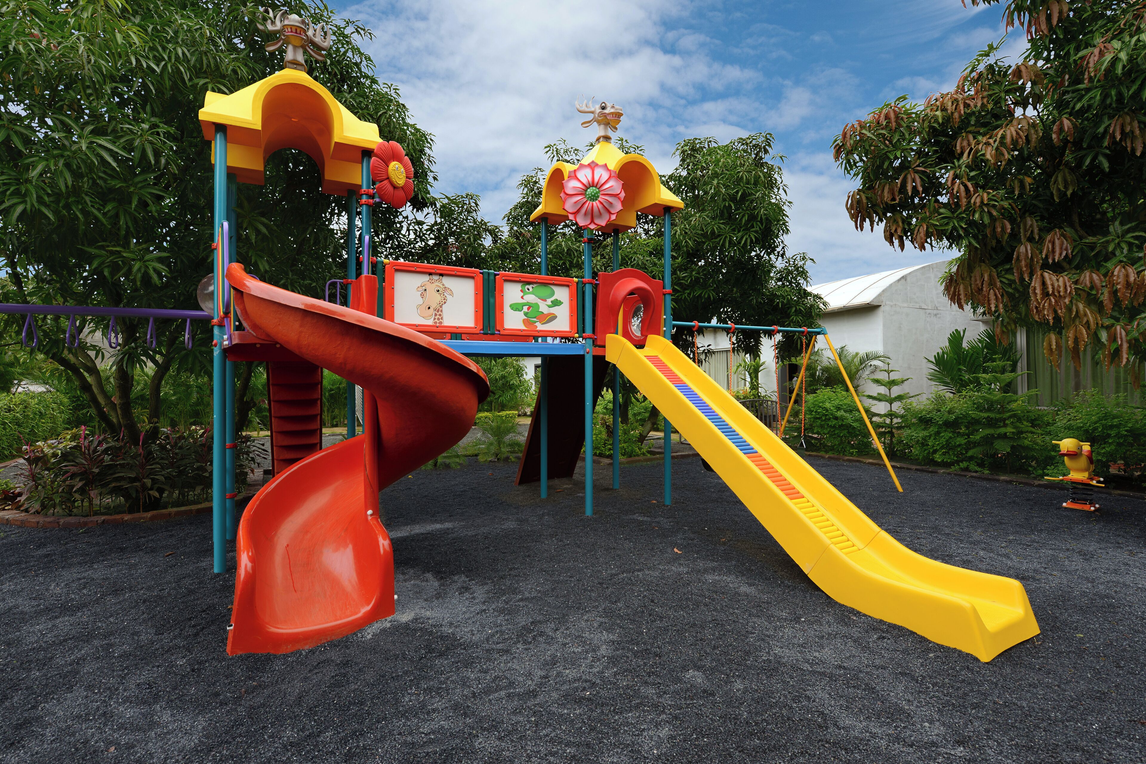 A playground with a red and yellow slide, surrounded by greenery.