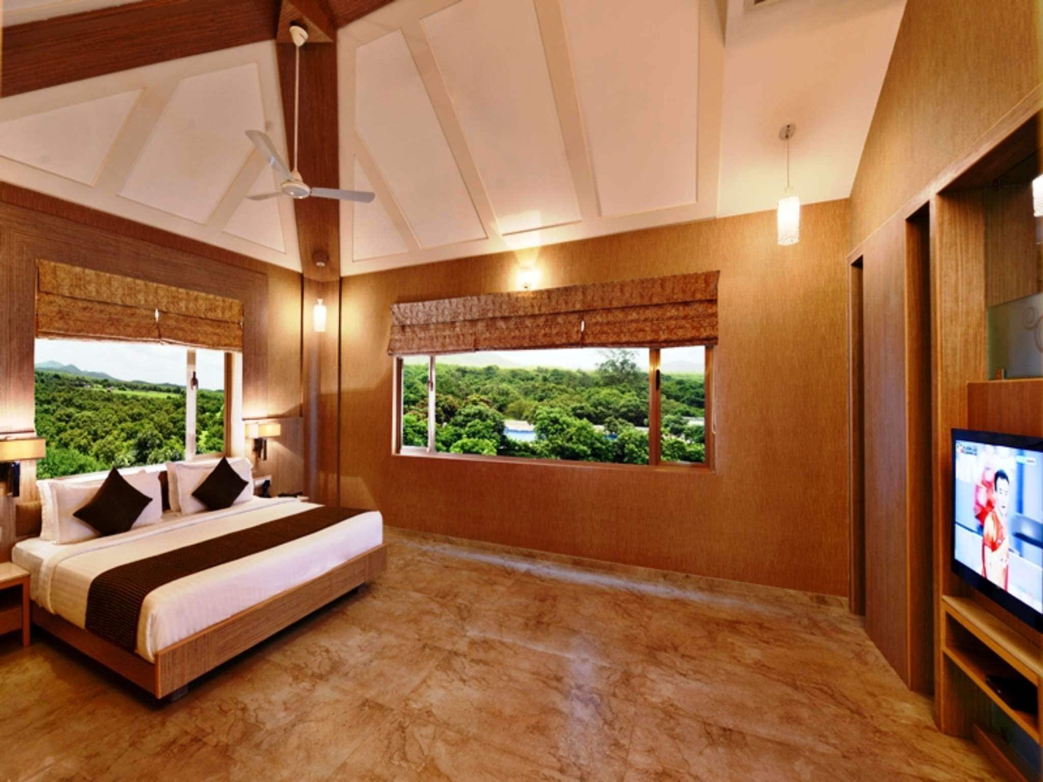 A hotel room with a bed, a television, and a view of a green landscape.