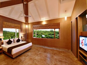 A hotel room with a bed, a television, and a view of a green landscape. - Sarovar Portico Gir (Mendarda)