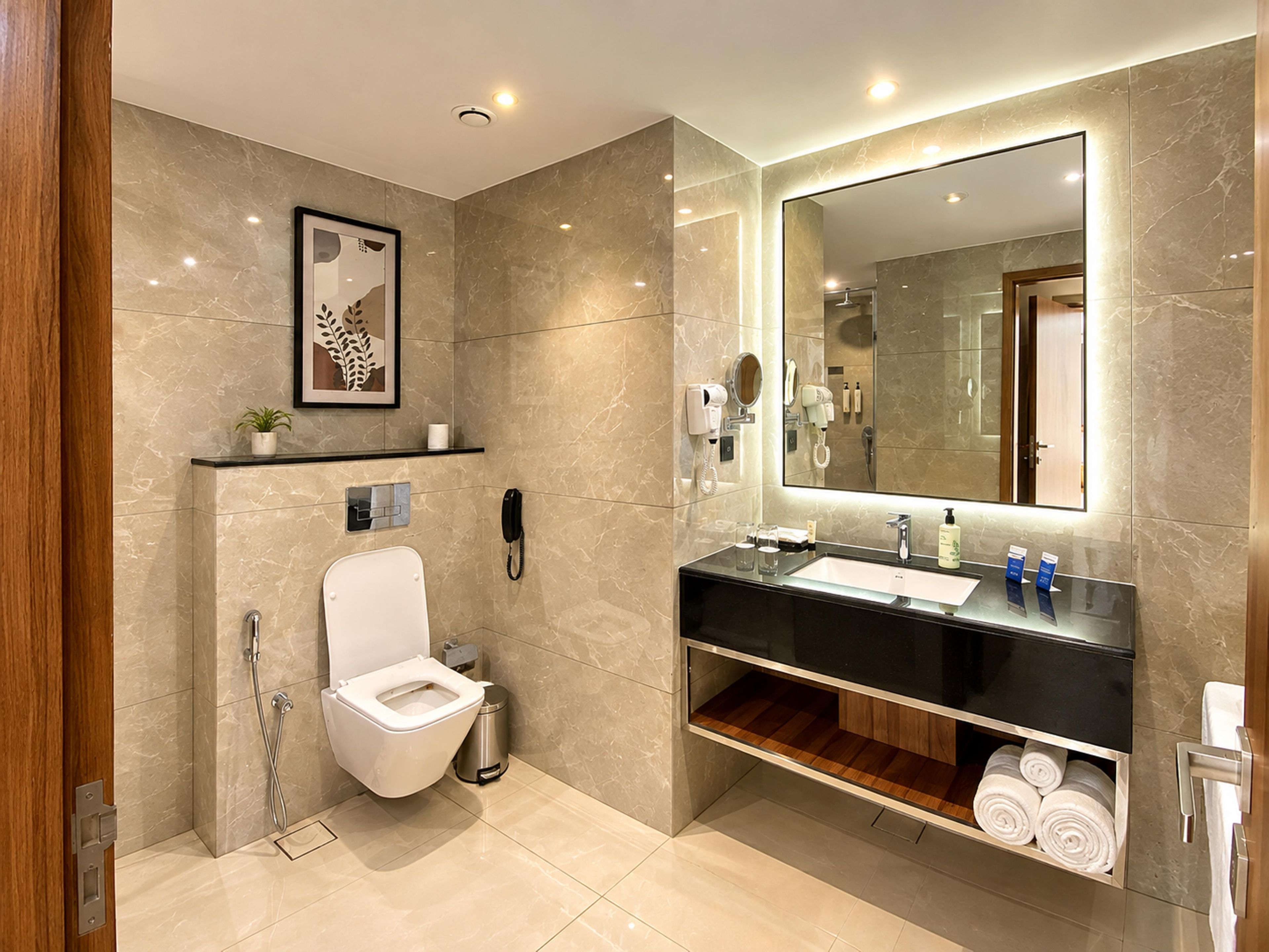 A modern bathroom with a toilet, sink, mirror, and a shelf with toiletries.