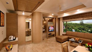 A modern hotel room with a large window offering a scenic view, a cozy seating area, a flat-screen TV, and a small kitchenette. - Sarovar Portico Gir (Mendarda)