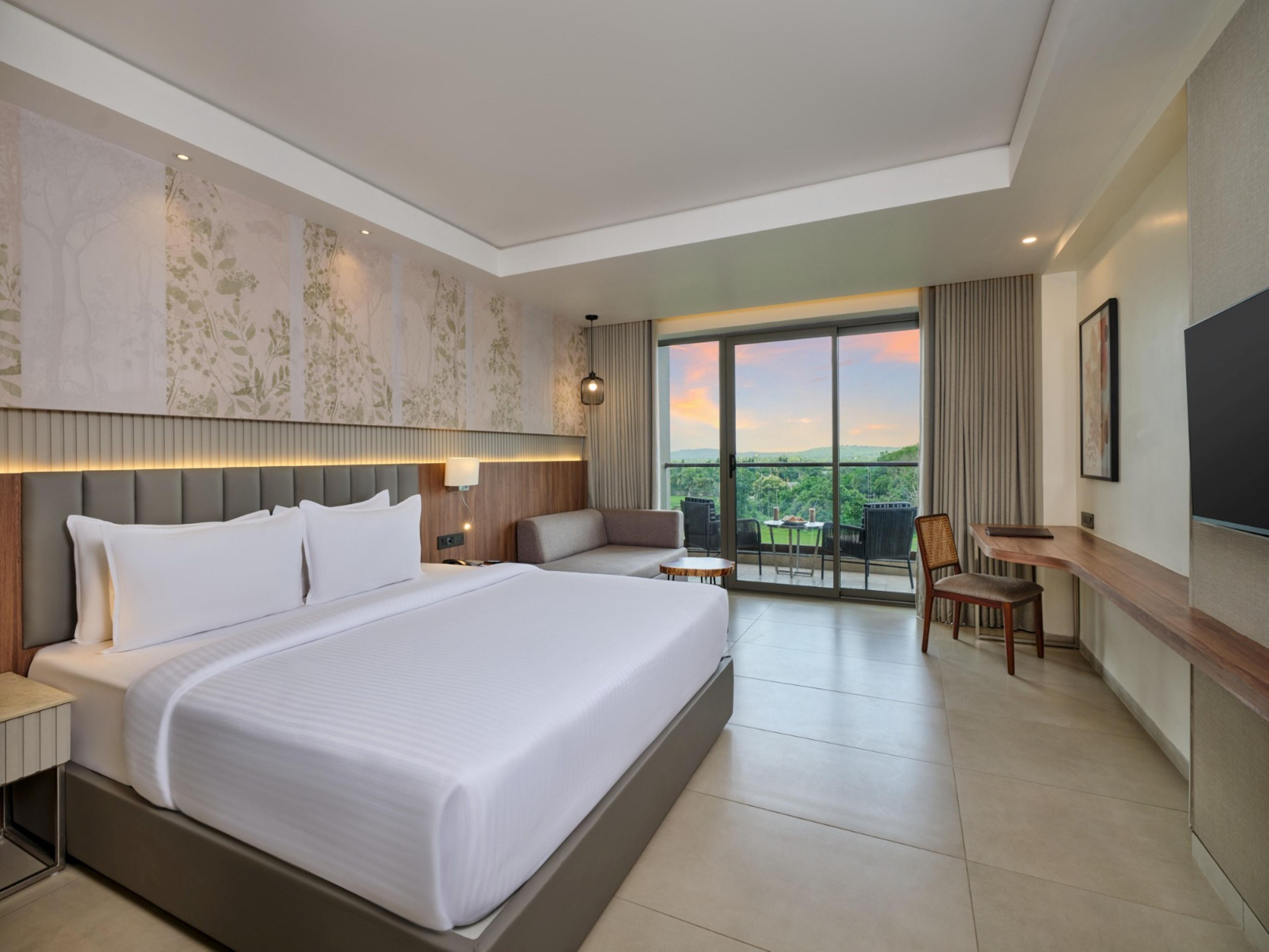 A hotel room with a large bed, a desk, a chair, and a view of the outdoors.