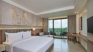 A modern hotel room with a large bed, a seating area with a sofa and chairs, a desk, and a balcony with a view. - Sarovar Portico Gir (Mendarda)