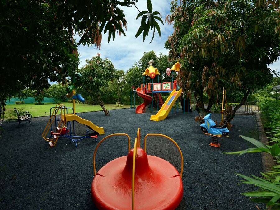 Ein Spielplatz mit verschiedenen Spielgeräten, darunter Rutschen und Schaukeln, umgeben von Bäumen und Grünflächen.